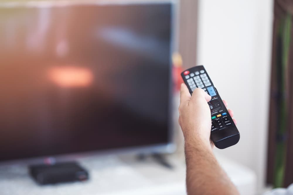 A Person Is Holding A Remote Control In Front Of A Television — Coastwide Antennas In Erina, NSW
