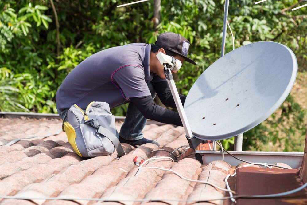 A Man Is Installing A Satellite Dish On The Roof Of A House — Coastwide Antennas In Ourimbah, NSW