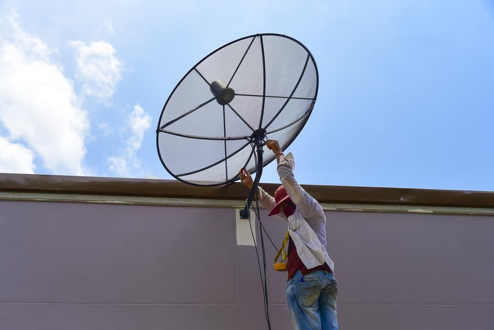 A Man Is Installing A Satellite Dish On The Roof Of A Building — Coastwide Antennas In Ourimbah, NSW