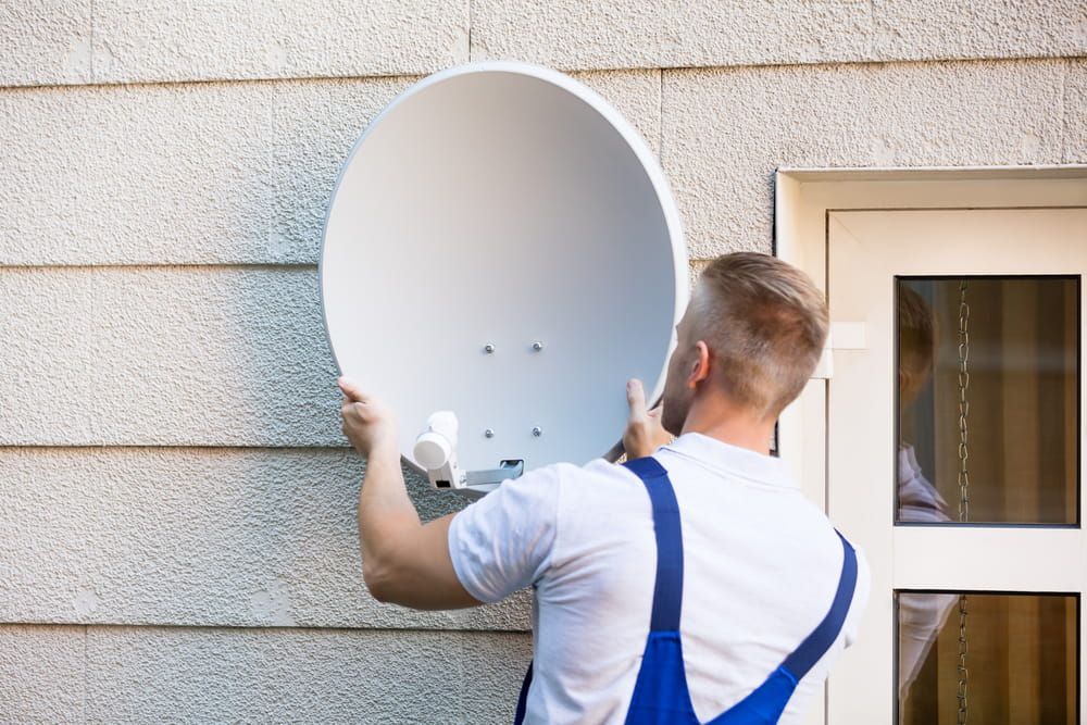 A Man Is Installing A Satellite Dish On The Side Of A Building — Coastwide Antennas In Ourimbah, NSW