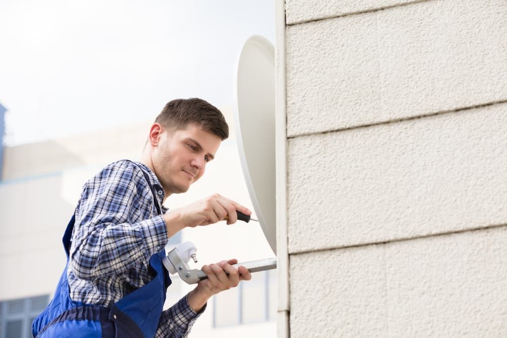 A Man Is Installing A Satellite Dish On The Side Of A Building — Coastwide Antennas In Terrigal, NSW
